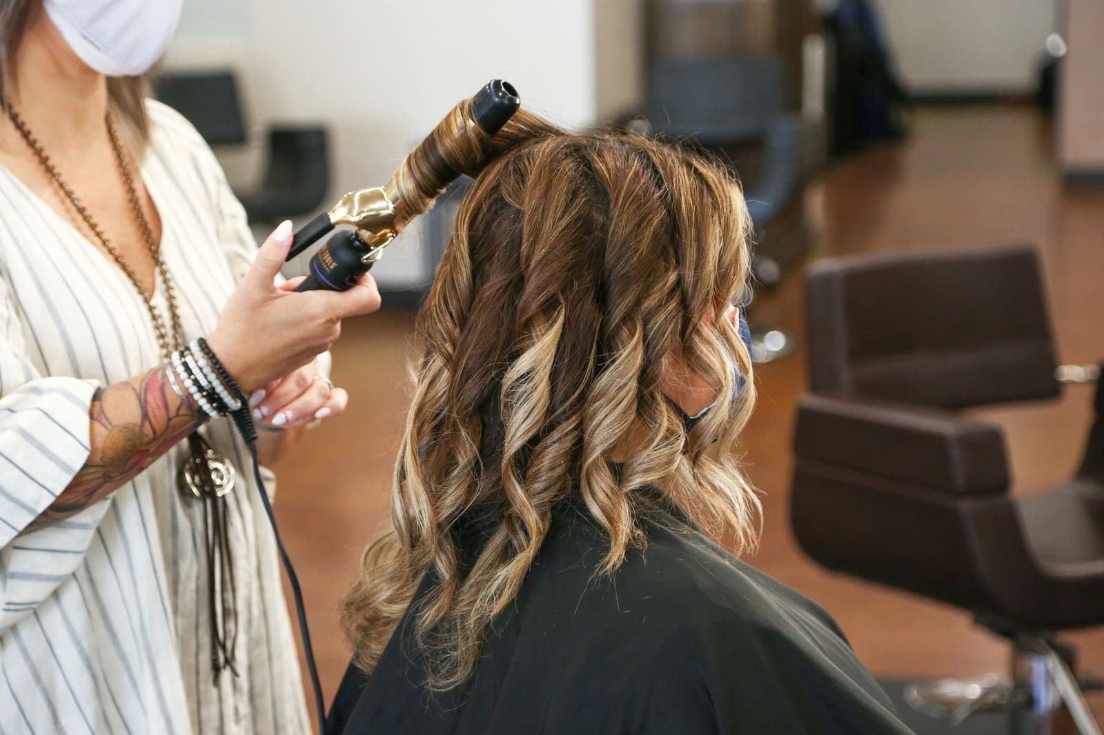 Coiffeuse créant des boucles au fer sur de longs cheveux méchés