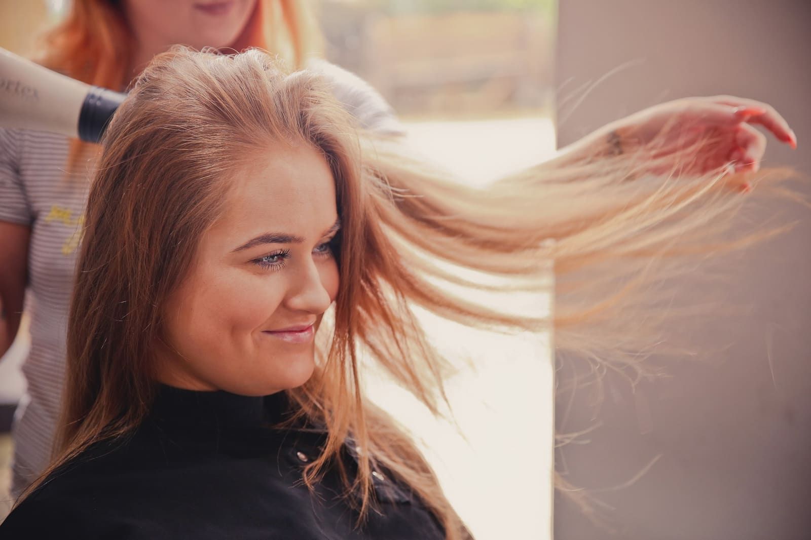 Coiffeuse donnant du mouvement à une longue chevelure rousse, en lumière douce