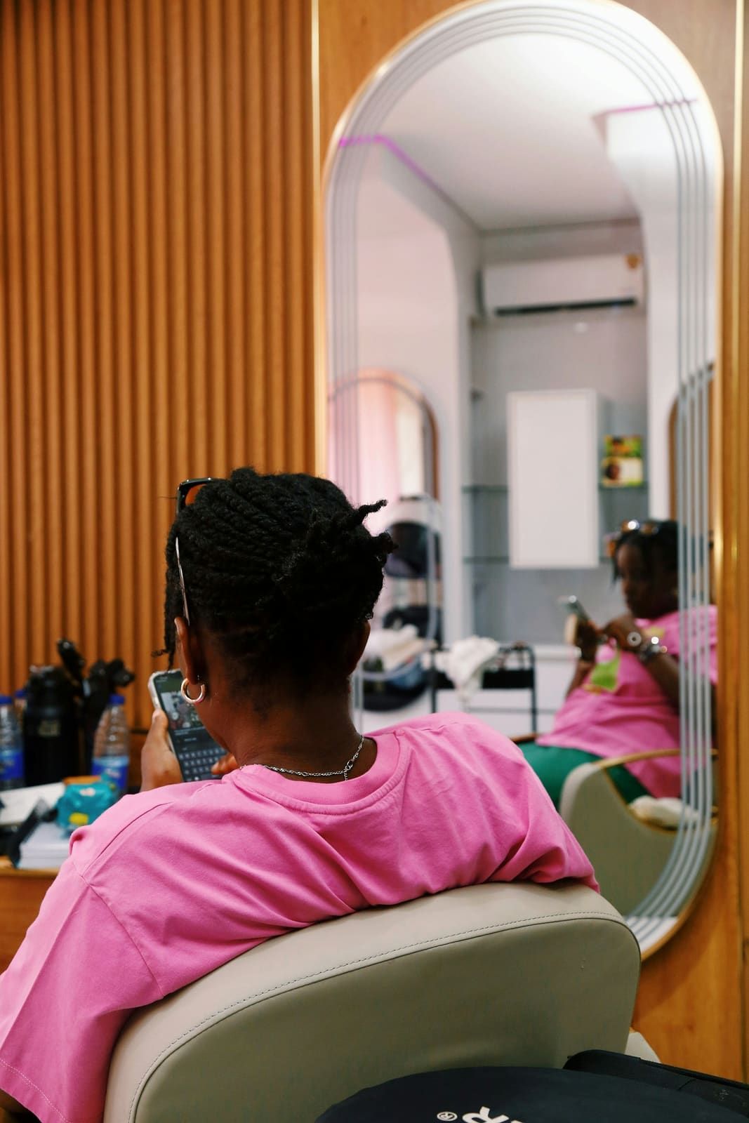 Cliente installée devant un grand miroir en arche, dans un salon aux tons roses